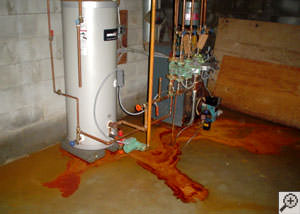Puddles of reddish, brown, and yellow iron ochre flooding on a basement floor near some utilities.
